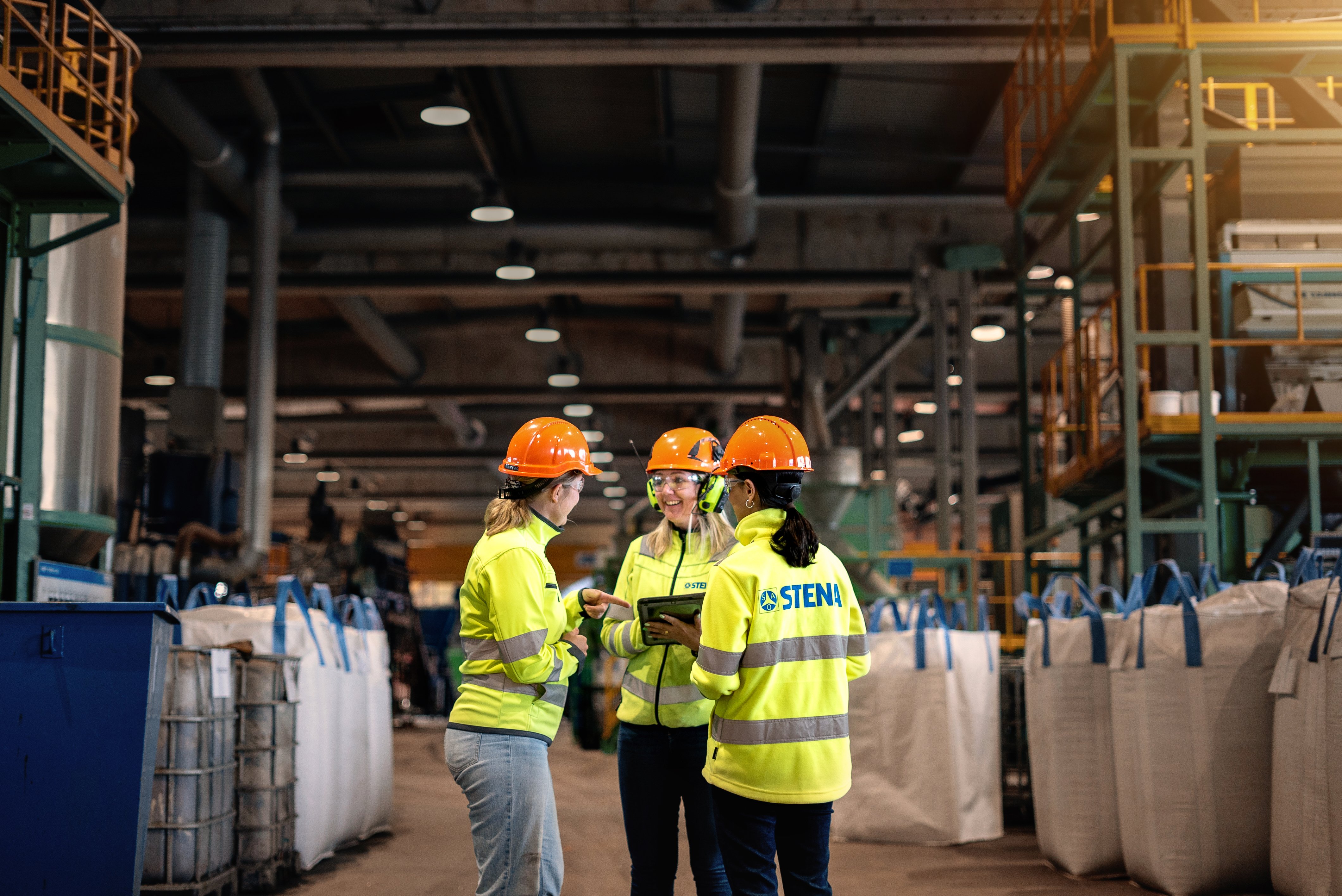 A group of three Stena Metall Group employees talk at Stena Nordic Recycling Center, Halmstad, Sweden.
